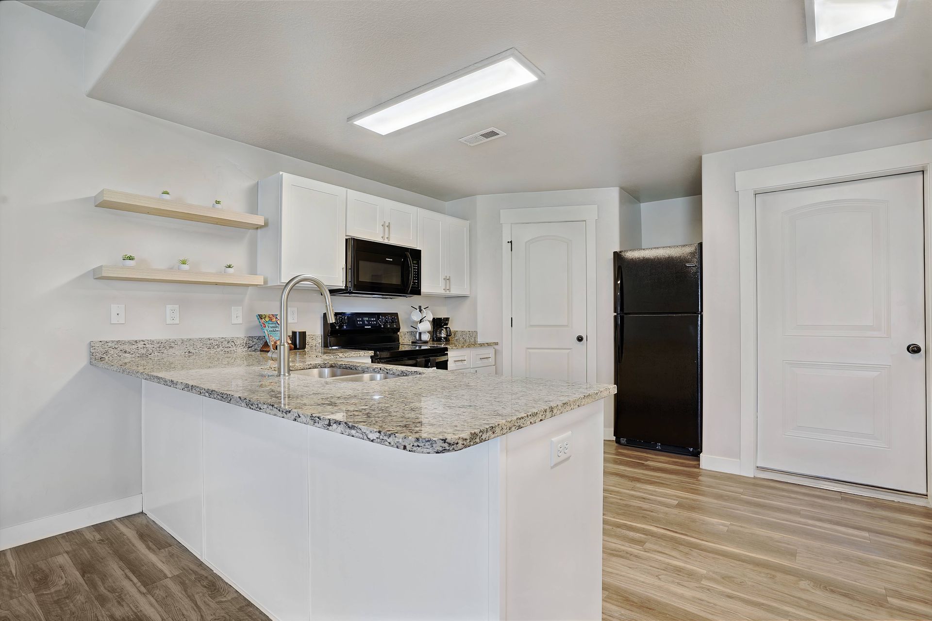 Kitchen with white cabinets, granite countertop, stainless steel sink, black appliances, and wood floor.