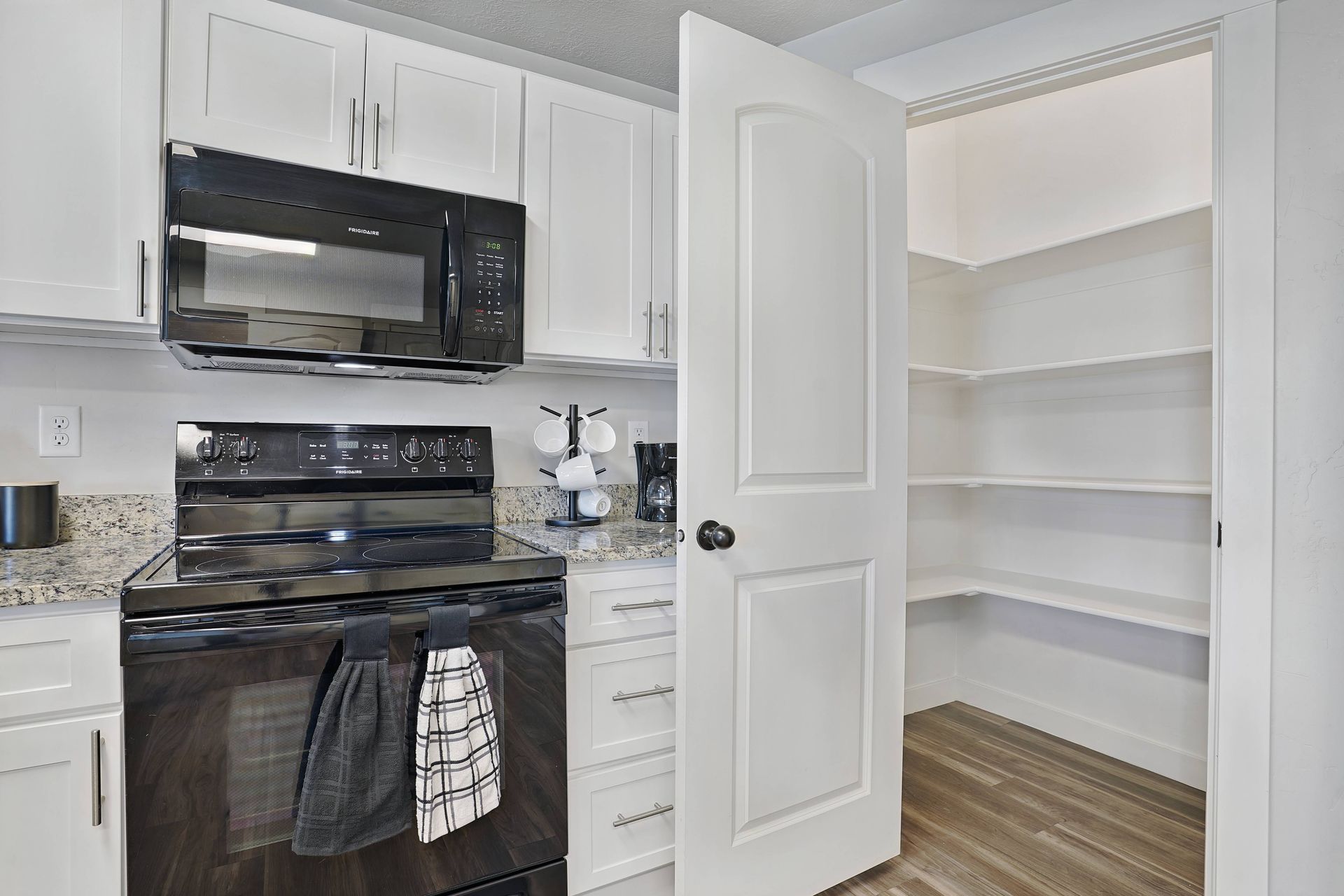 Kitchen with white cabinets, black appliances, and pantry with shelves.