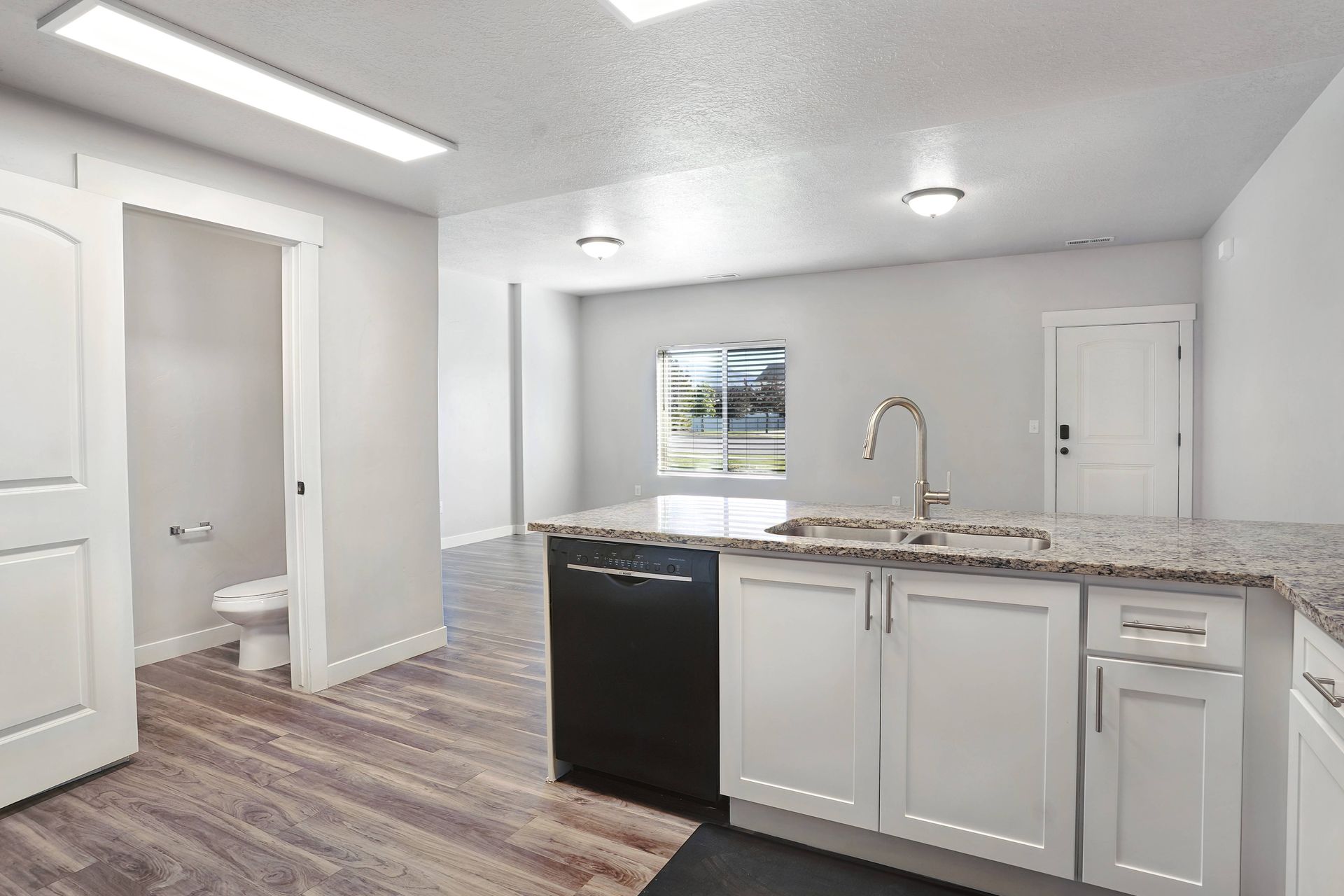 Kitchen with white cabinets, black appliances, granite countertop, and wood-look flooring.