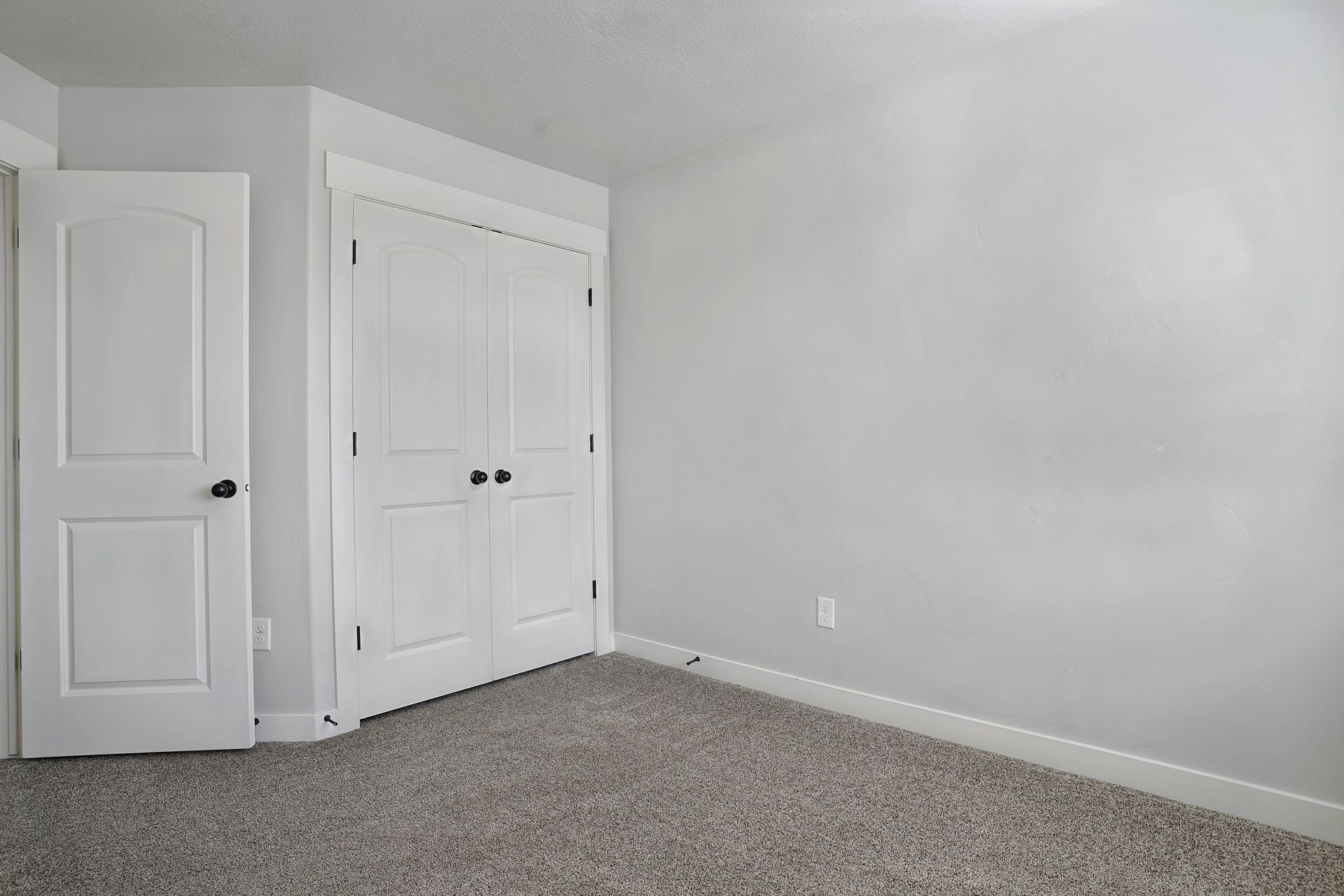 Empty room with gray walls, white doors, and a neutral carpet.