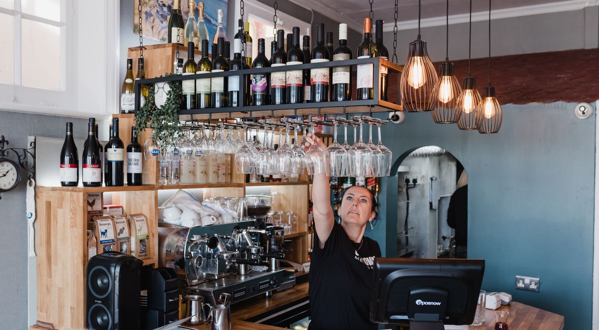 A woman is standing at a bar holding wine glasses over her head.
