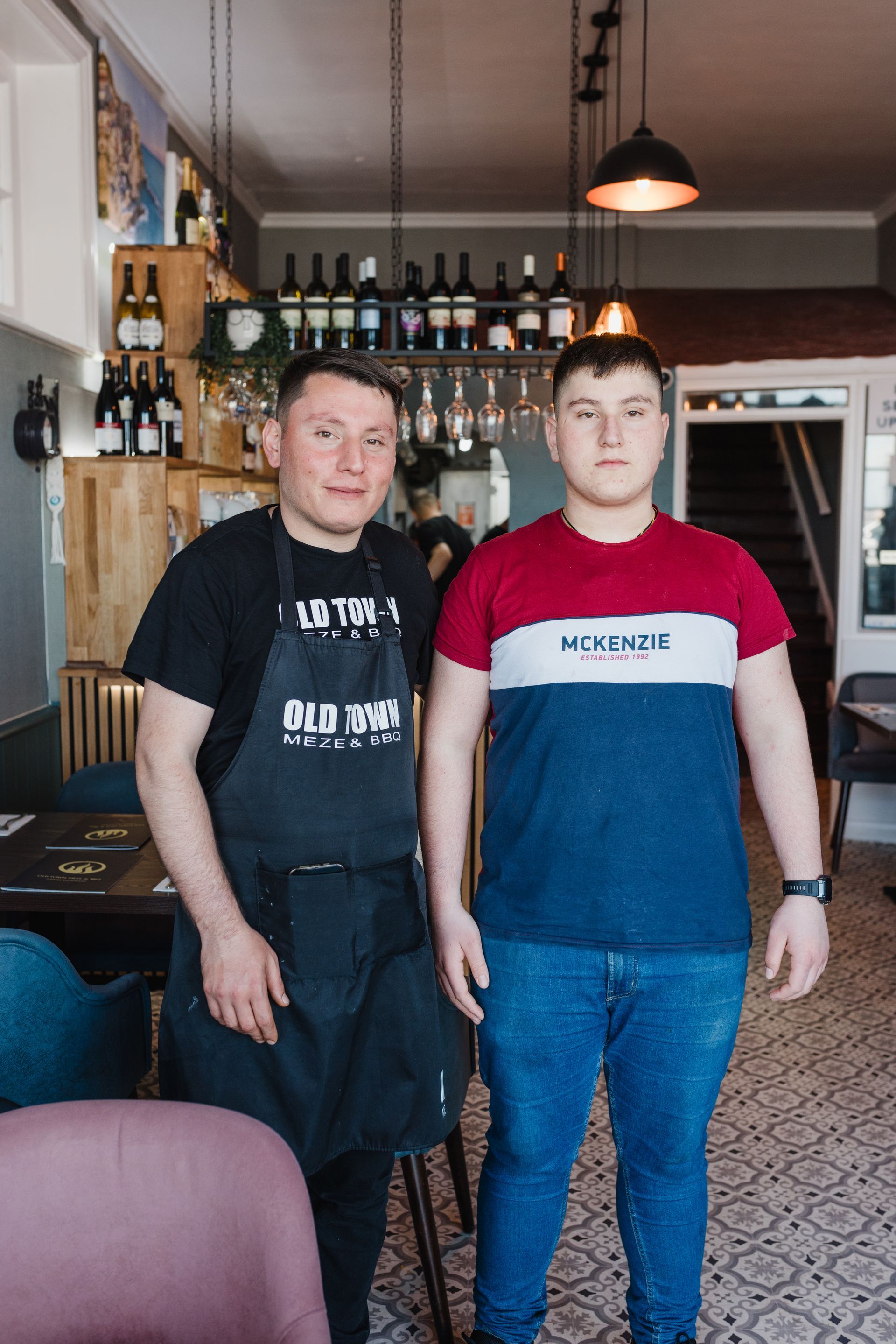 Two men standing next to each other in a restaurant with one wearing a shirt that says ' heinz ' on it