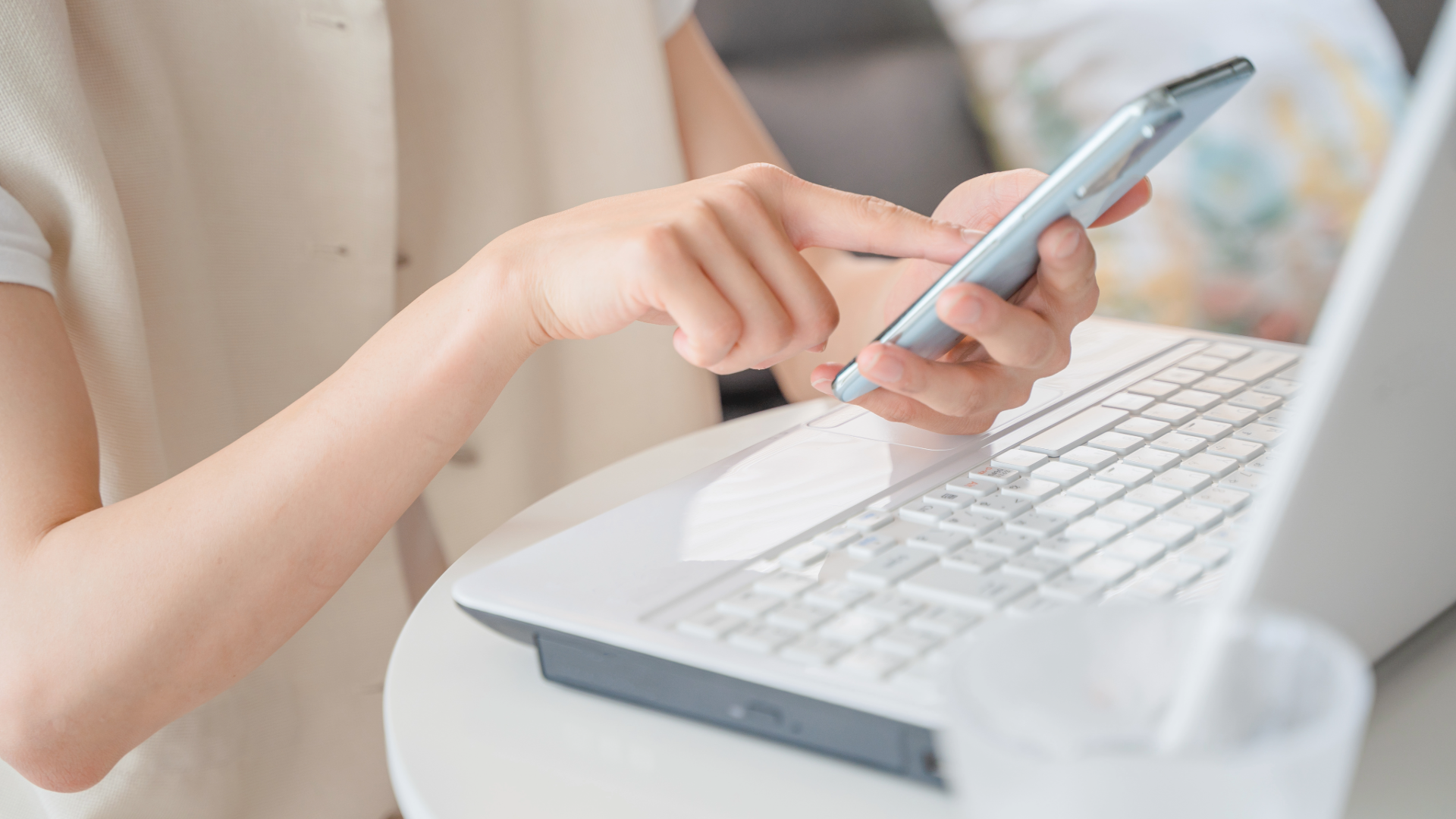 Hands using a smartphone beside a laptop keyboard on a desk