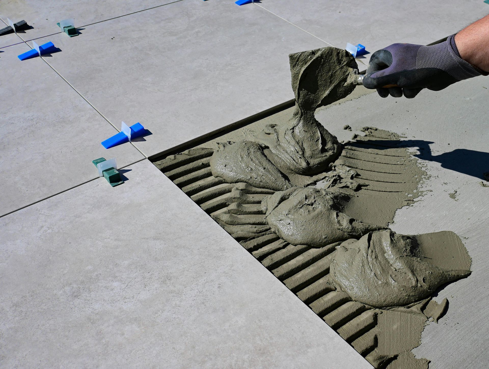 Person using a trowel to apply mortar to the floor for setting tiles, with leveling clips in place.