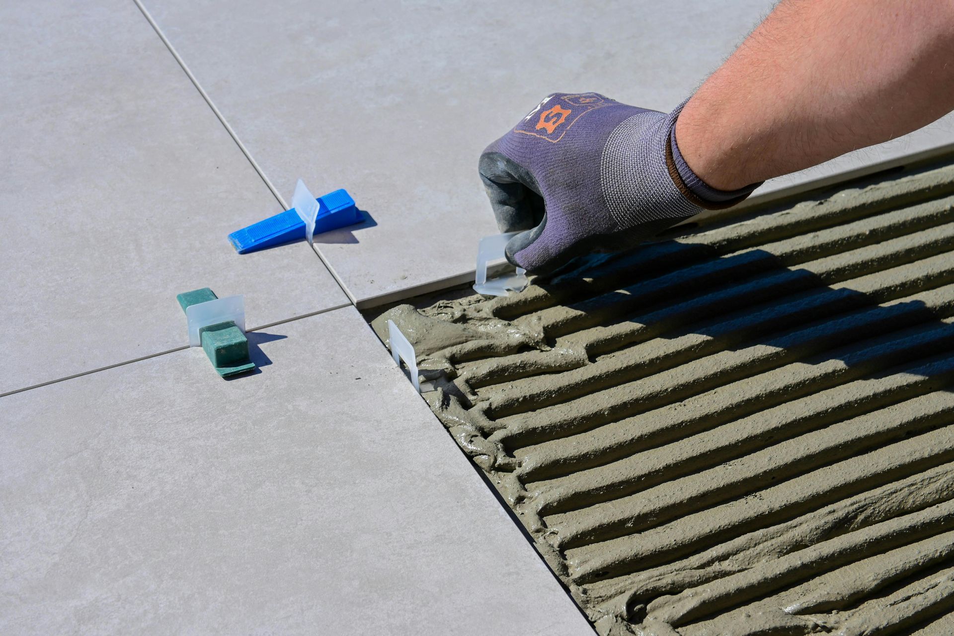 Person using tile leveling system to set ceramic tile. Hand wearing glove inserting clip.