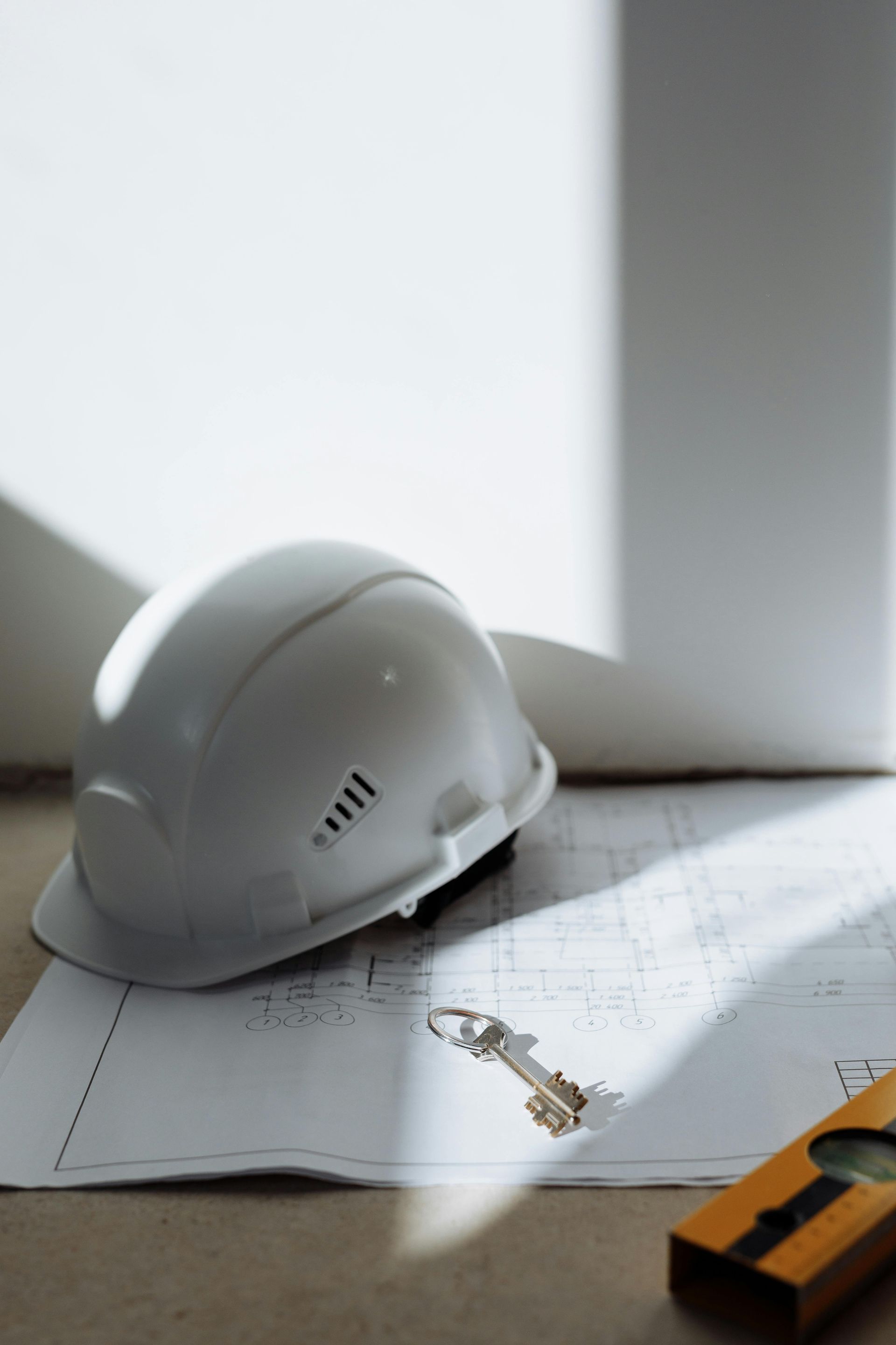 White hard hat and keys resting on a blueprint near a level.