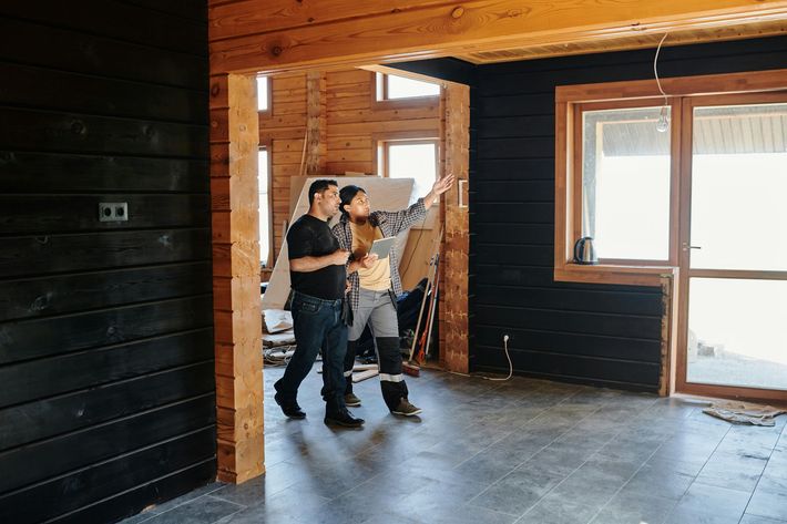 Two people in a partially finished house, one pointing at the window.
