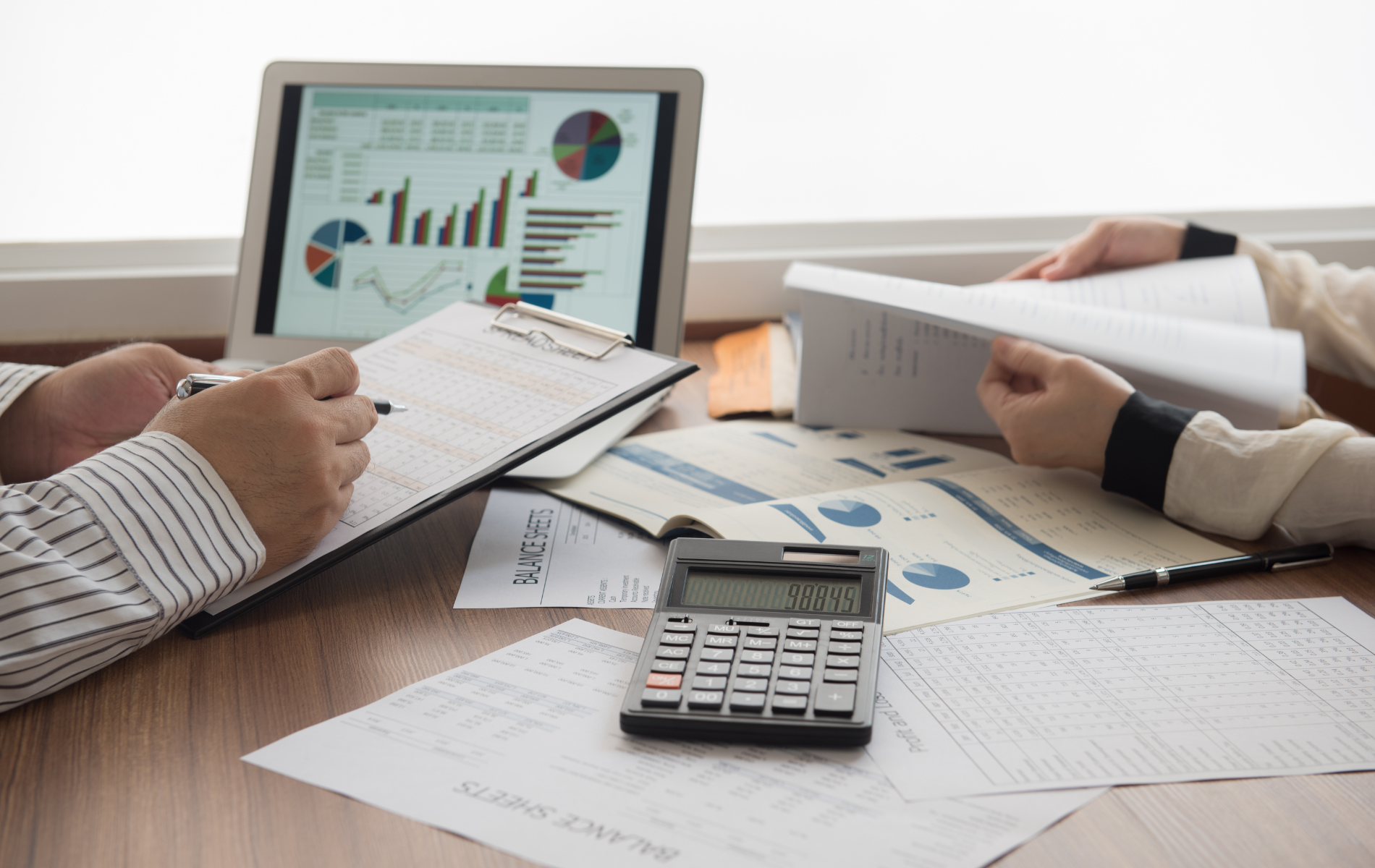 A man and a woman are sitting at a table looking at papers and a laptop.