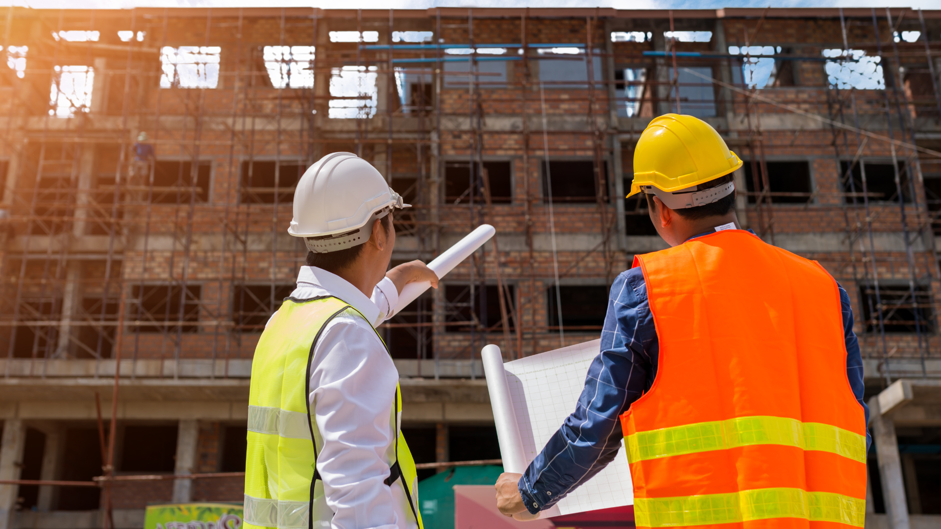 Two construction workers are looking at a blueprint at a construction site.