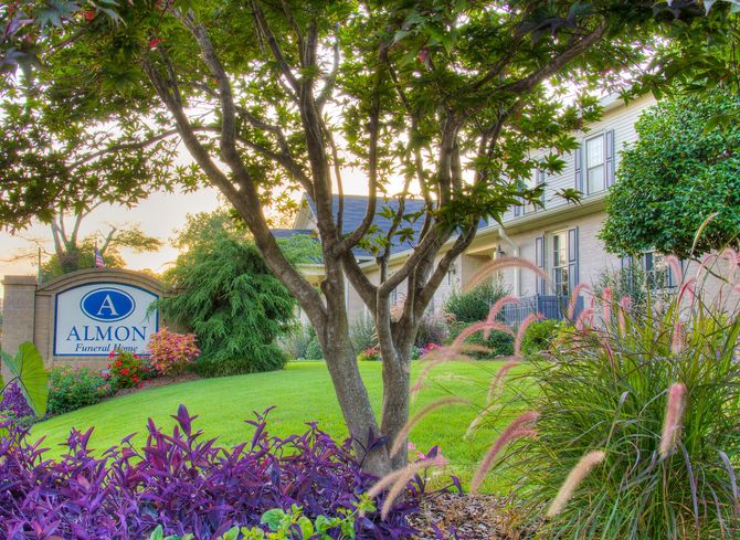Group of professionals posing outside the Almon building with a landscaped lawn and sign.