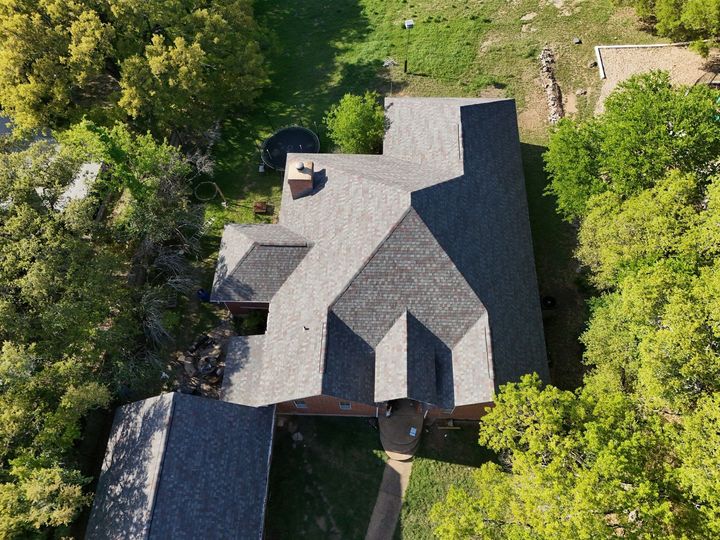 Overhead view of a house with a gray roof, surrounded by green trees and grass.