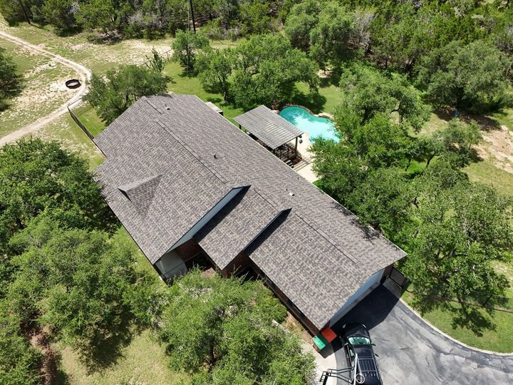 Aerial view of a house with a brown shingle roof, surrounded by green trees and a driveway.