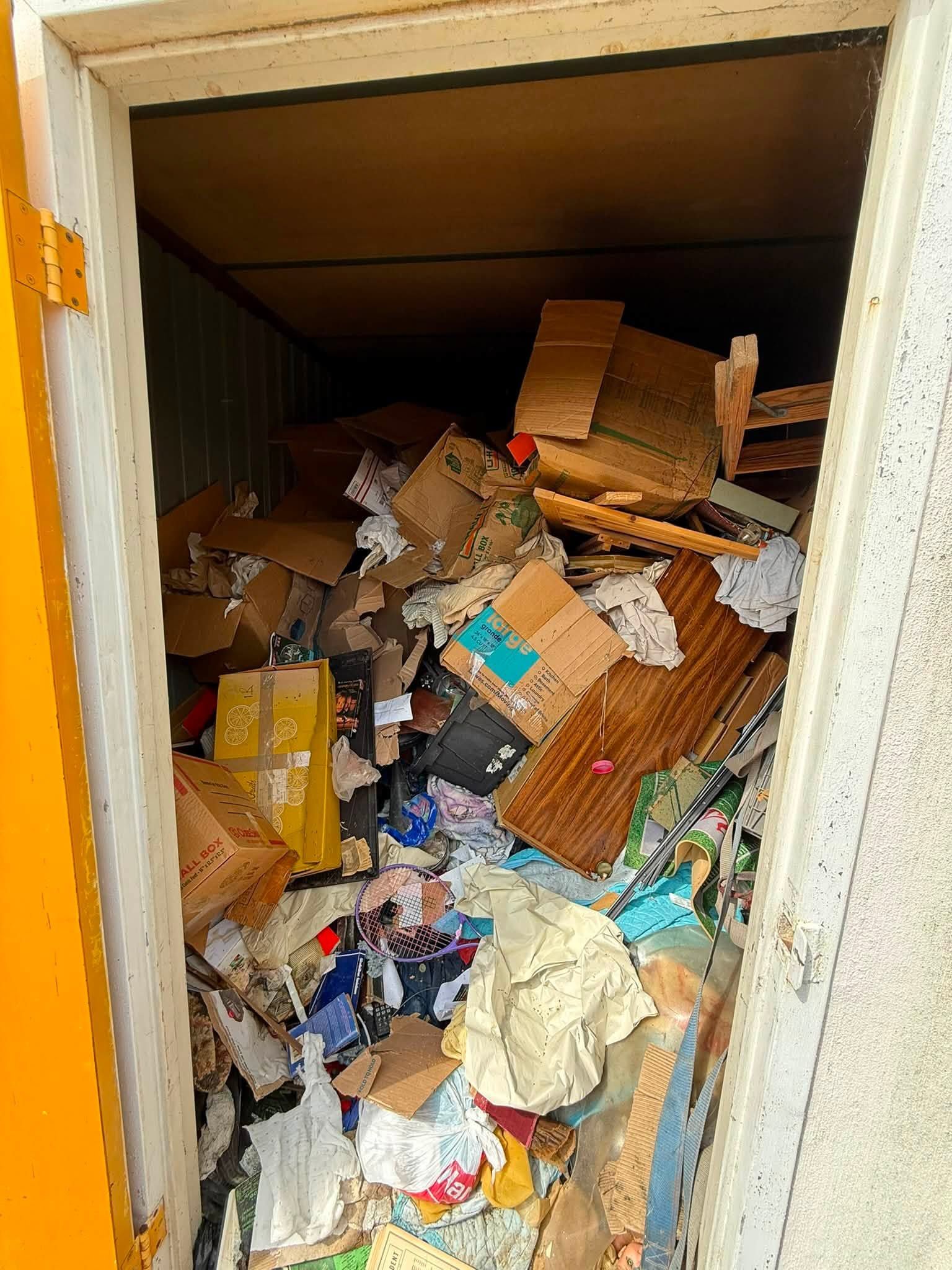 Overflowing storage closet filled with piles of cardboard, papers, and miscellaneous clutter