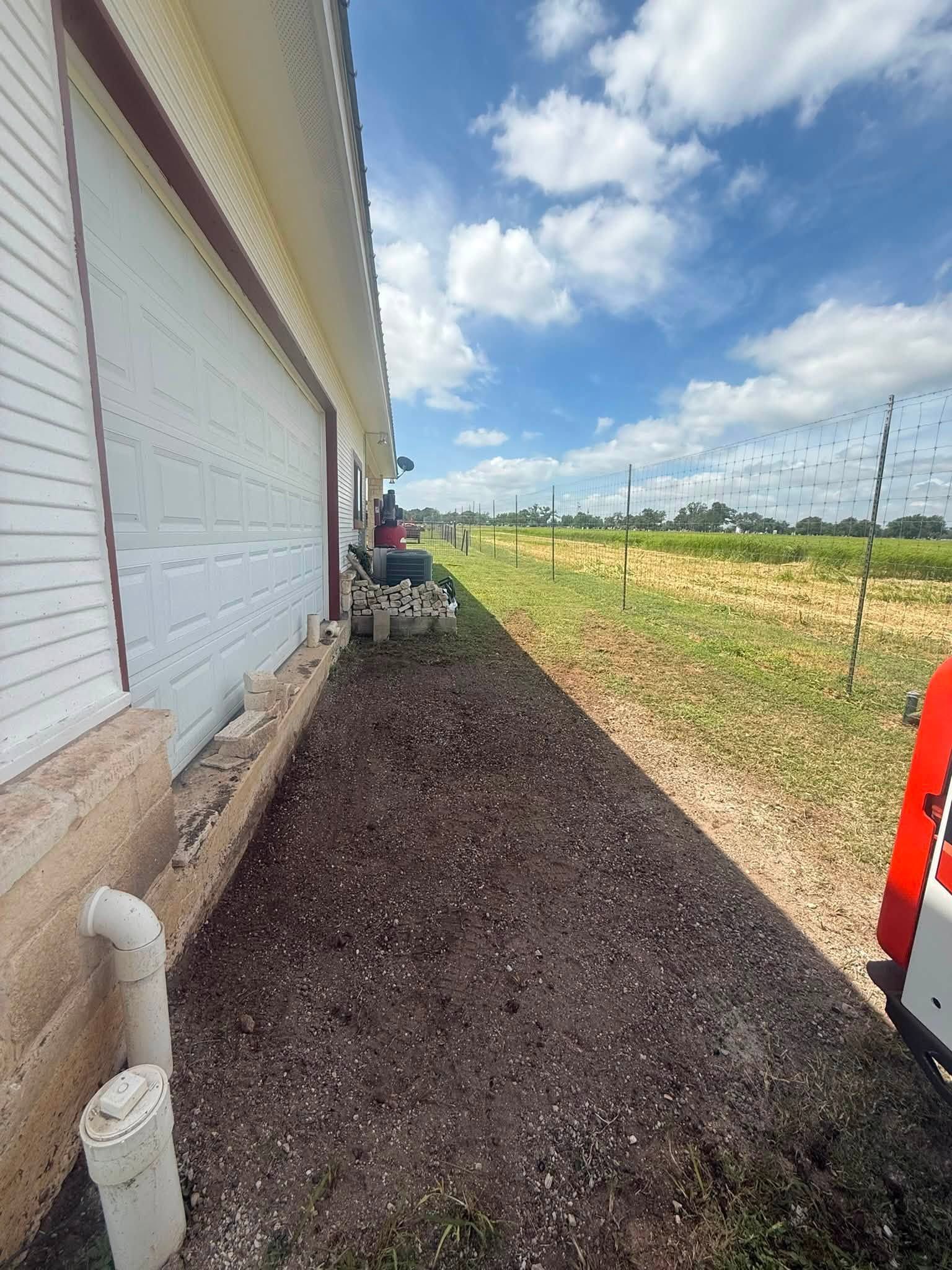 Gravel strip beside white building under blue sky, with fields and utility poles in the distance.