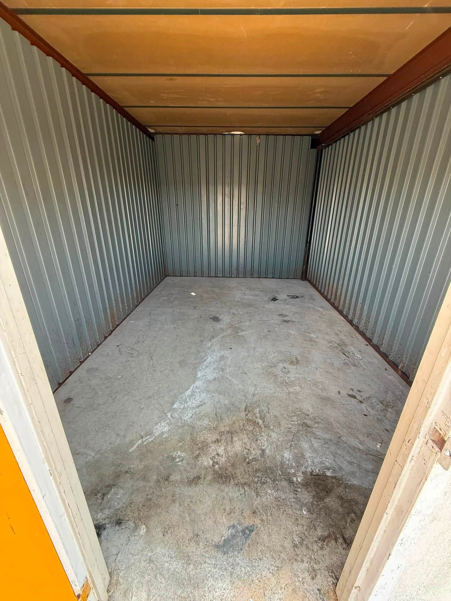 Empty corrugated metal storage shed with a concrete floor and wooden ceiling, viewed through an open doorway