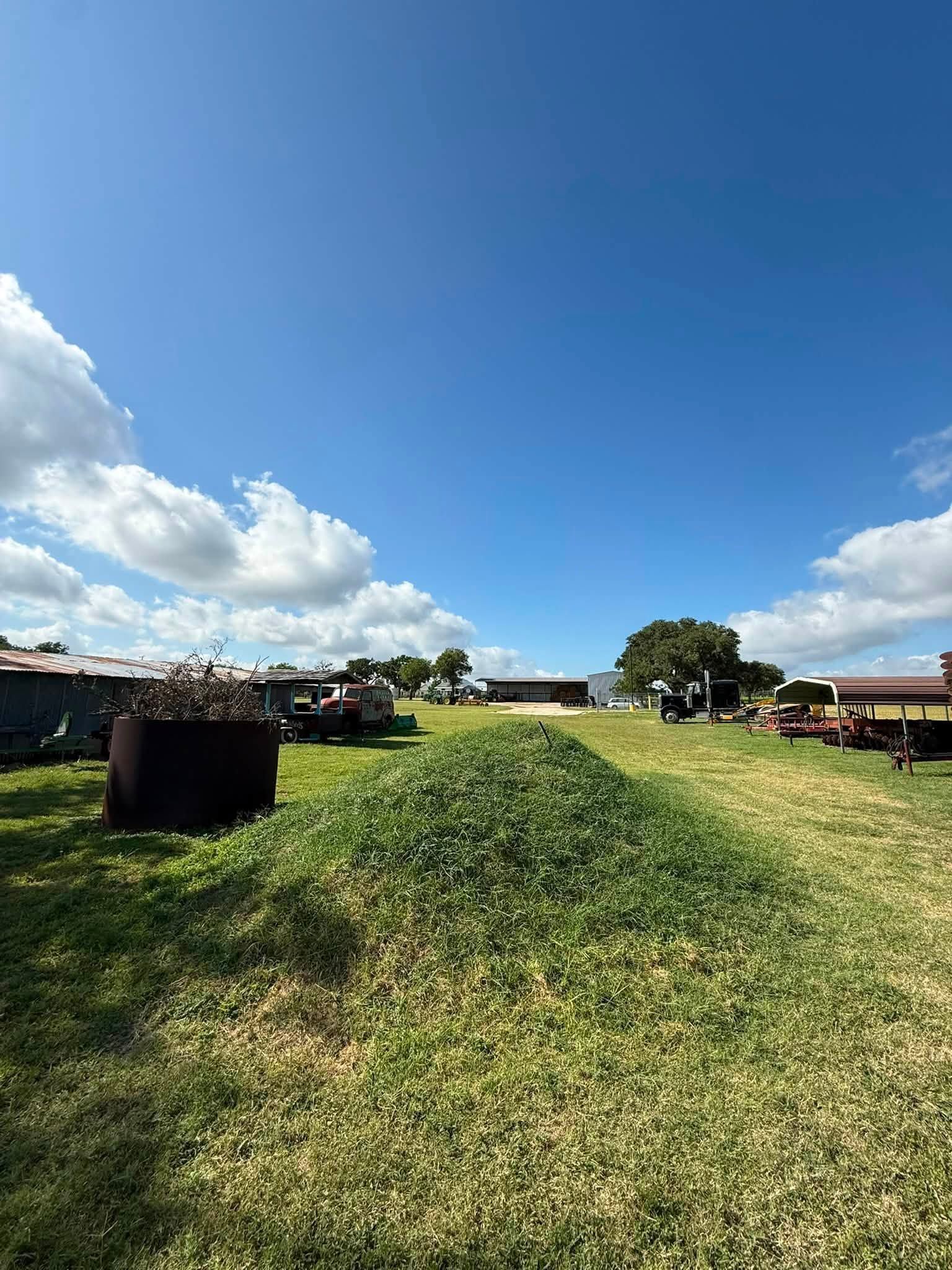 Open grassy path between hay bales under a bright blue sky with scattered clouds