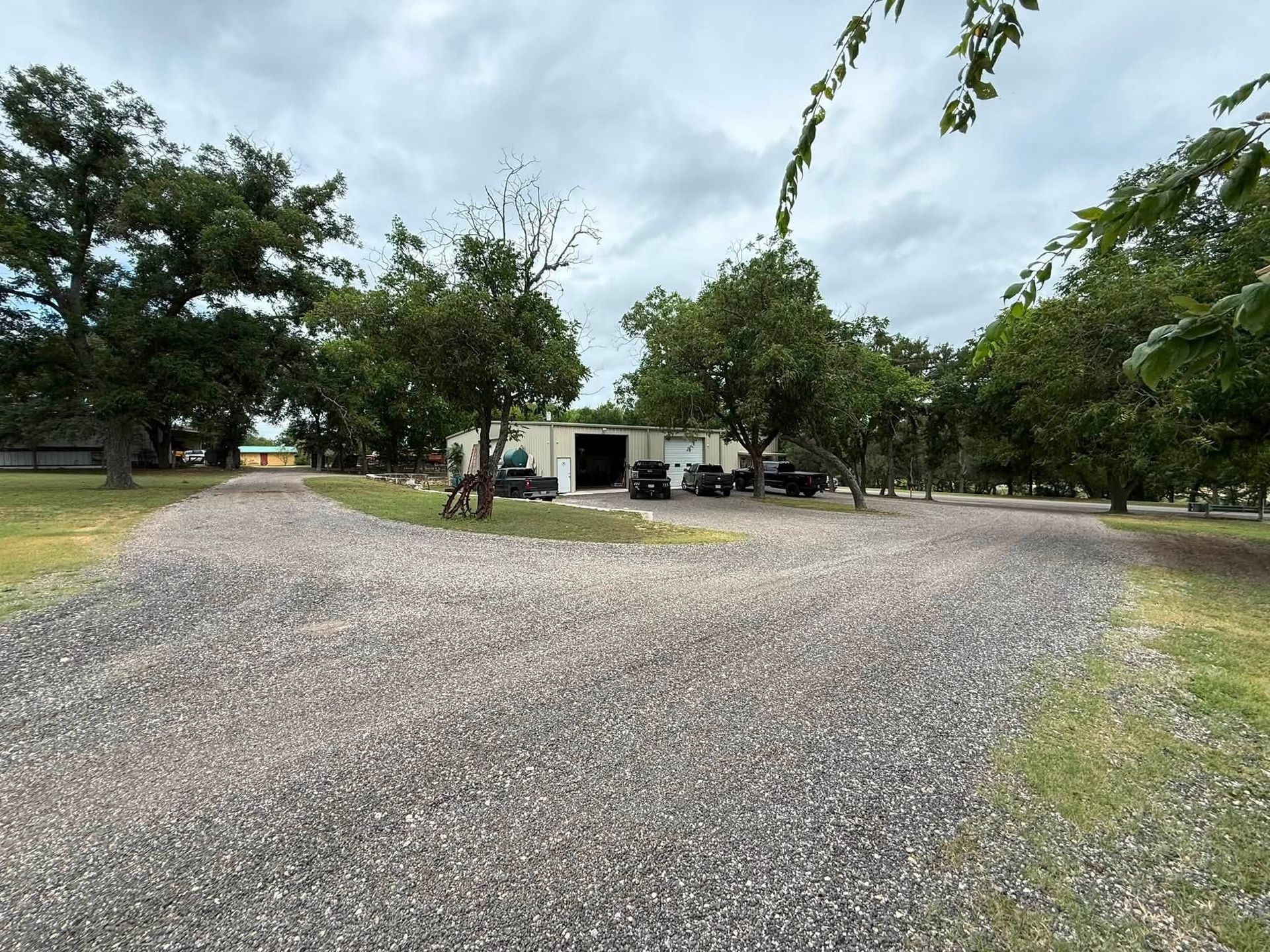 Gravel lot with a small building and trees under a cloudy sky