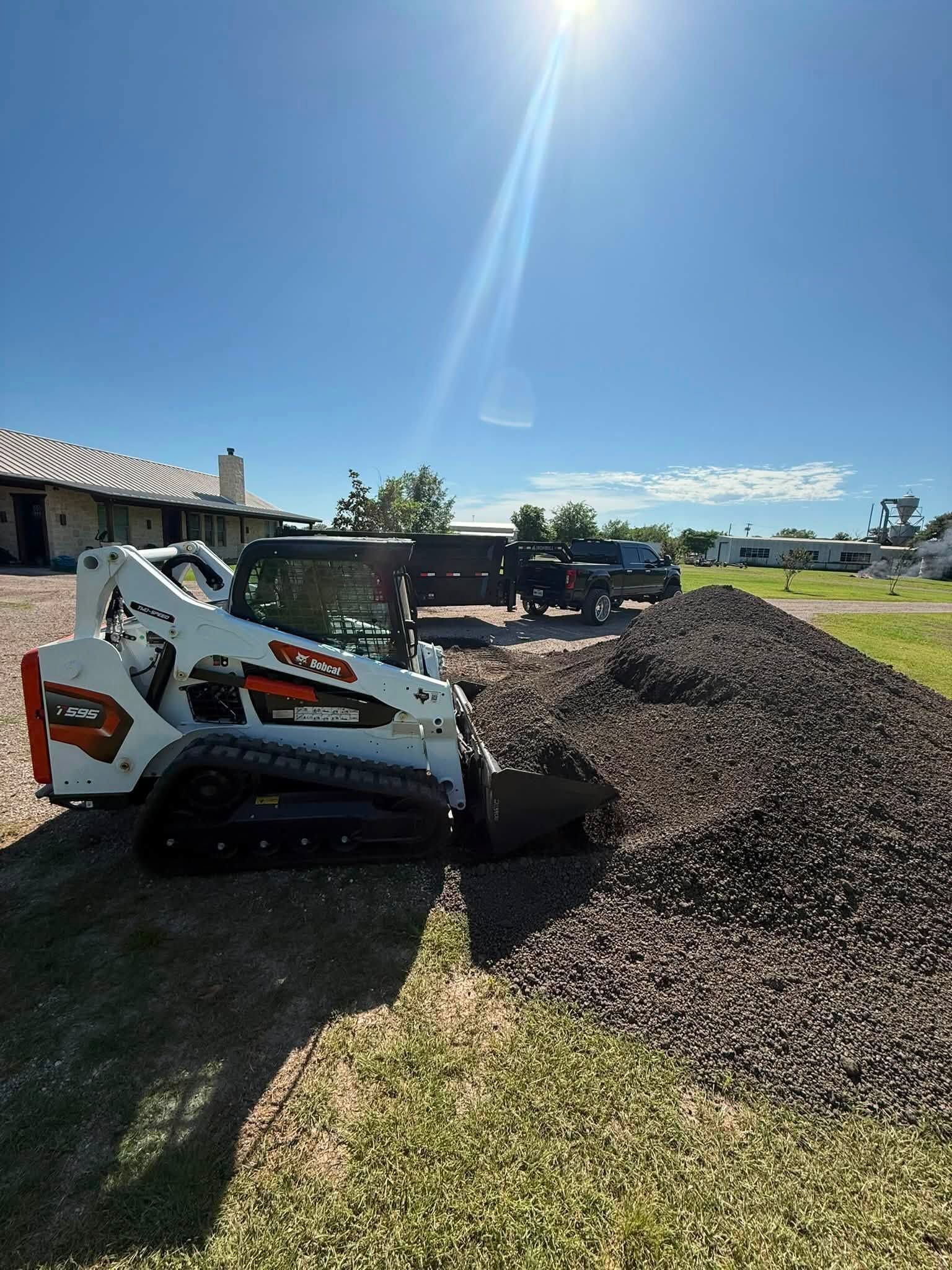 Bobcat skid steer pushing gravel in a residential driveway under bright sun