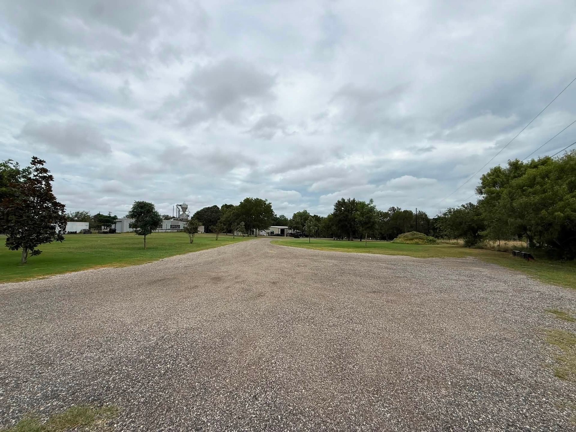 Wide gravel path through a grassy park under a cloudy sky
