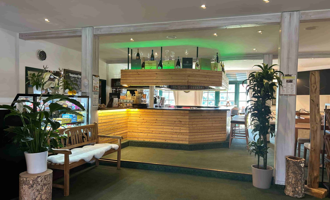 Die Bar des Restaurant Platzhirsch in Olching mit Hockern und grüner Beleuchtung. Links eine Holzbank und die Snackthecke