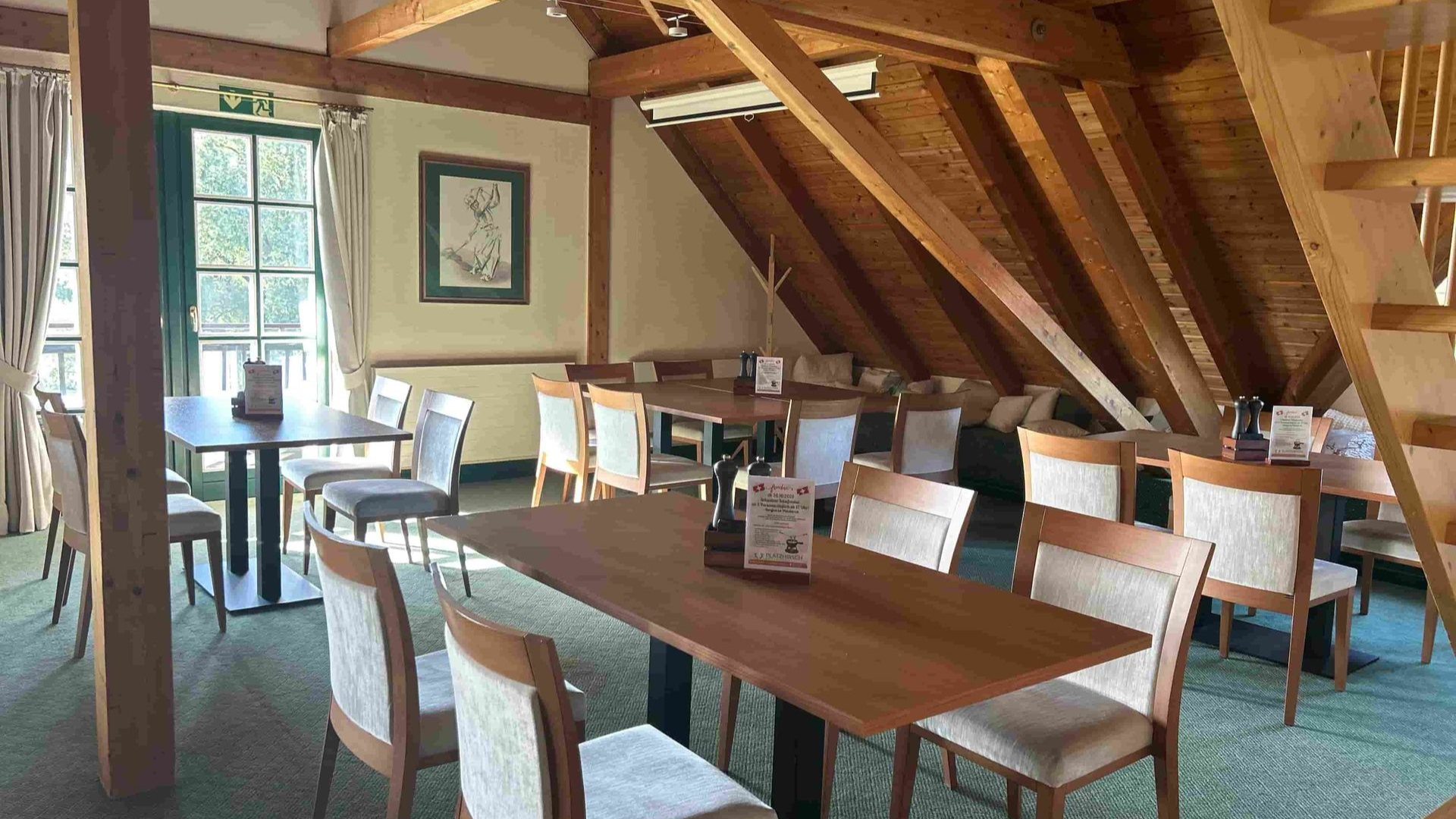 Blick in den Event- und Tagungsraum des Restaurant Olching, man sieht Tische und Stühle zwischen Dachstreben