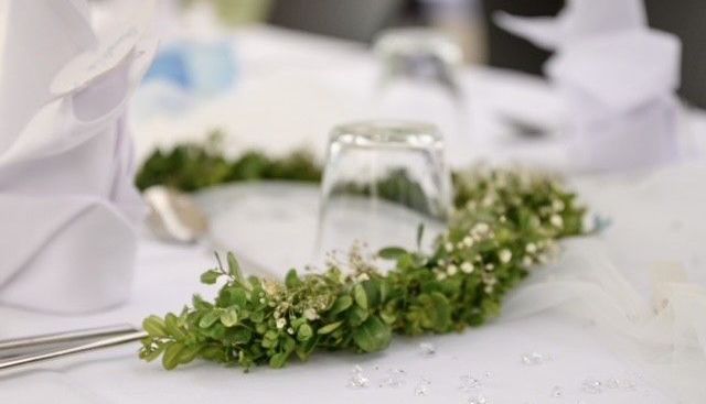 Feierlicher Tischschmuck, ein Kranz aus Zweigen mit kleinen Blüten liegt auf einem gedeckten Tisch auf der Terrasse