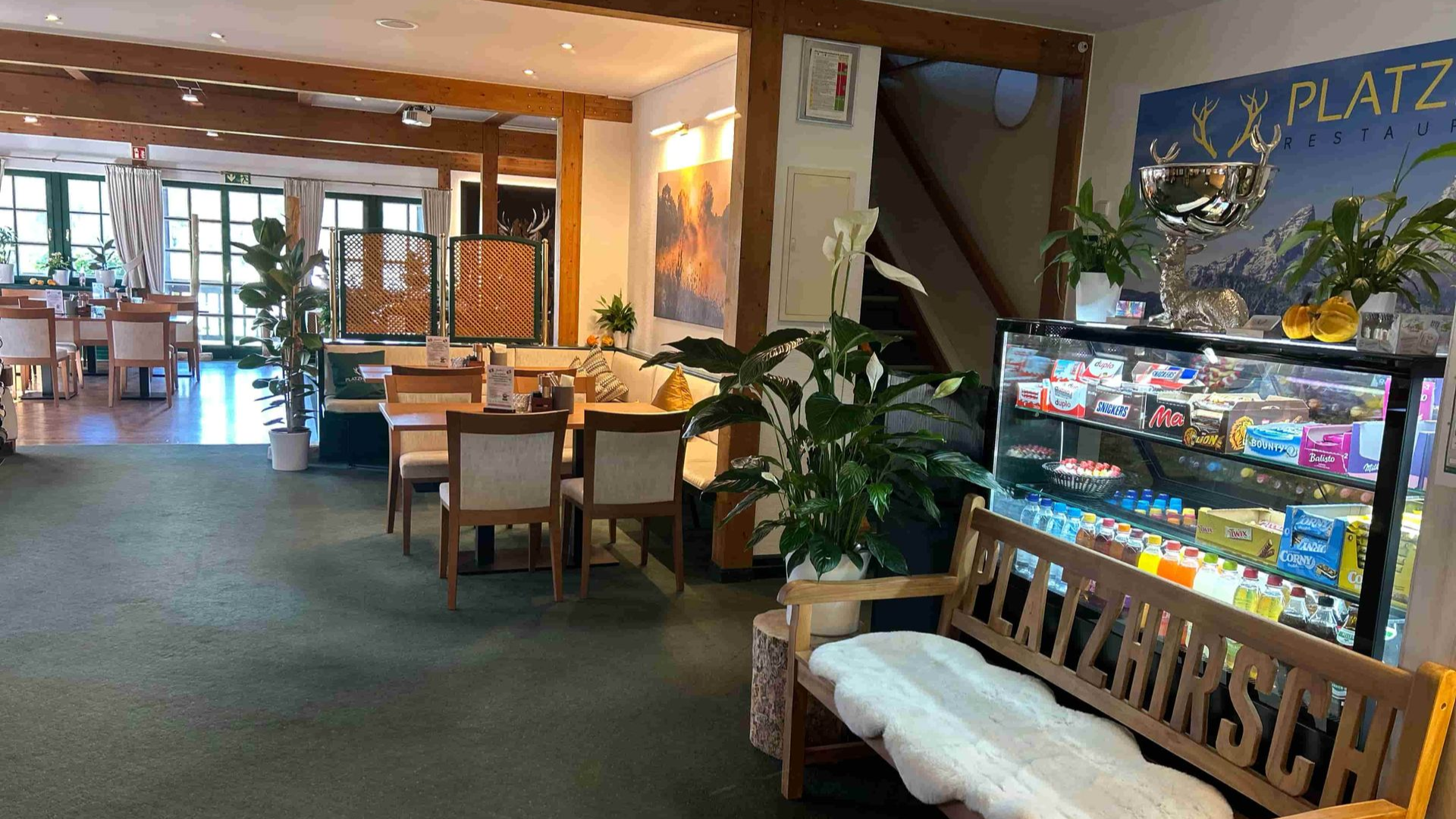 Die Snacktheke des Restaurant Olching, davor eine Holzbank. Links sind Tische und Stühle zu sehen