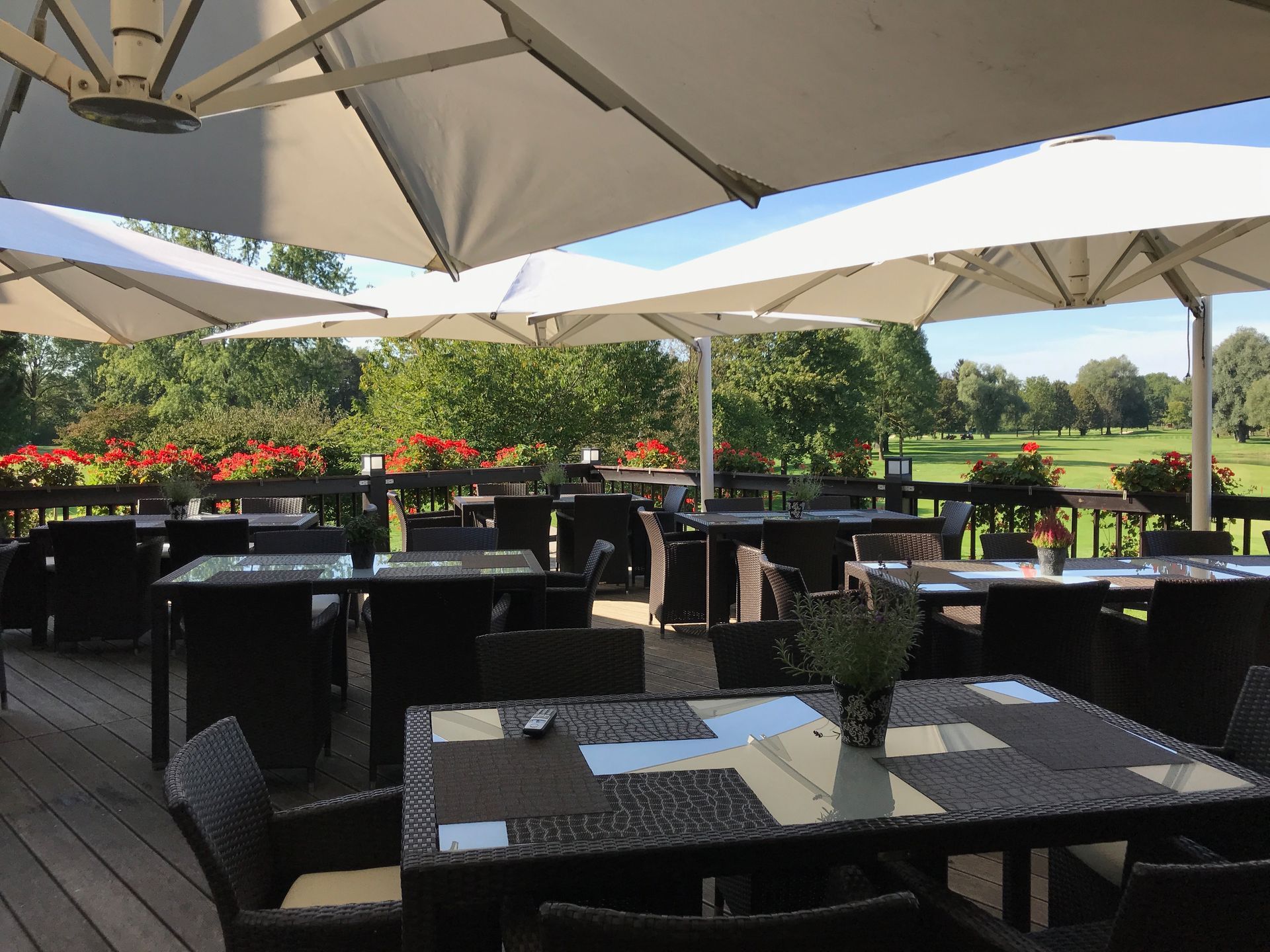 ein Restaurant mit Tischen und Stühlen unter Sonnenschirmen mit Blick auf einen Golfplatz.
