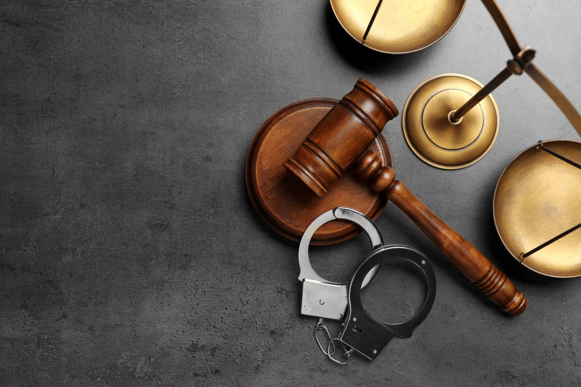 Gavel, handcuffs, and scales of justice arranged on a dark surface representing a legal case.
