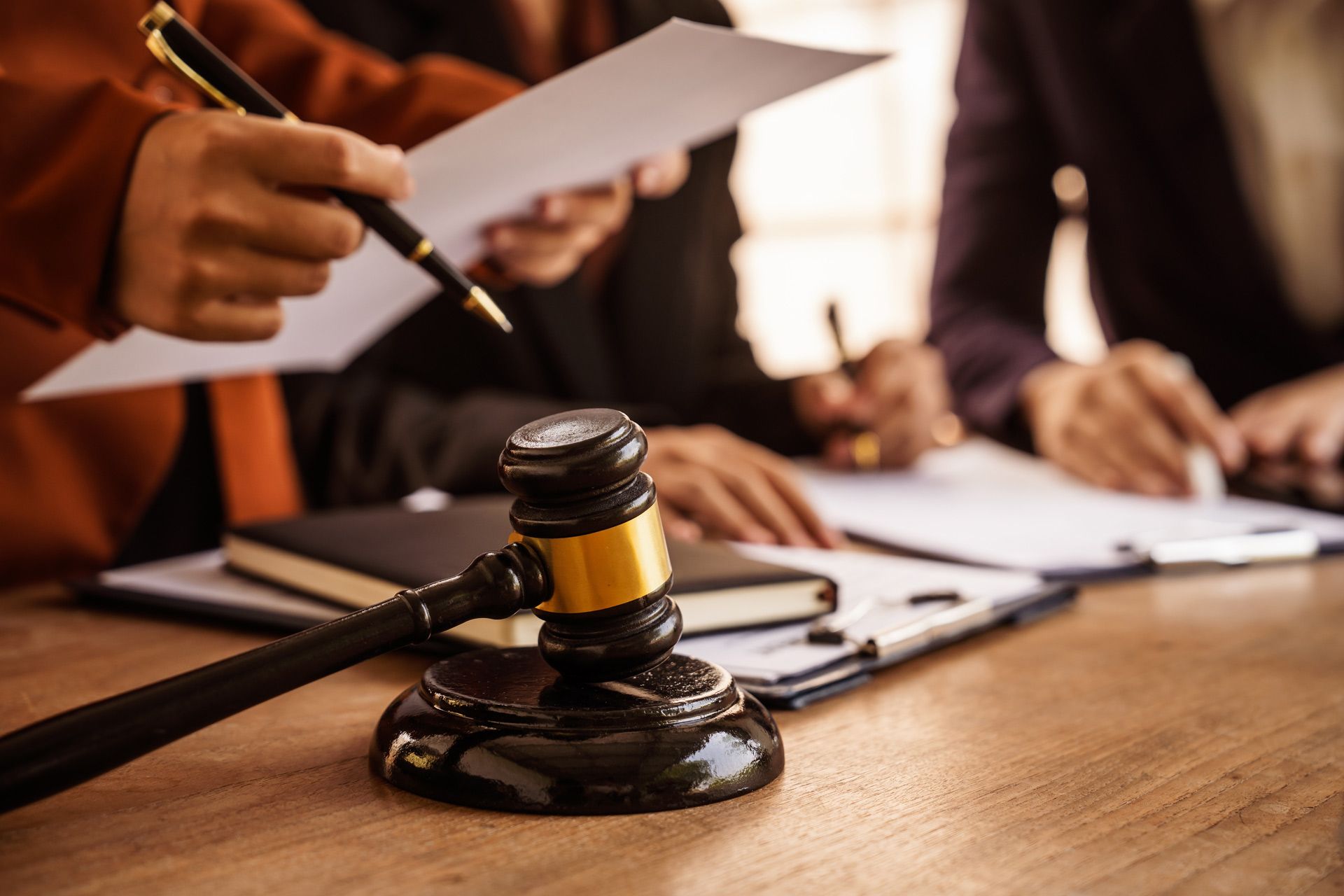 Judge’s gavel on a table as legal professionals review documents together.