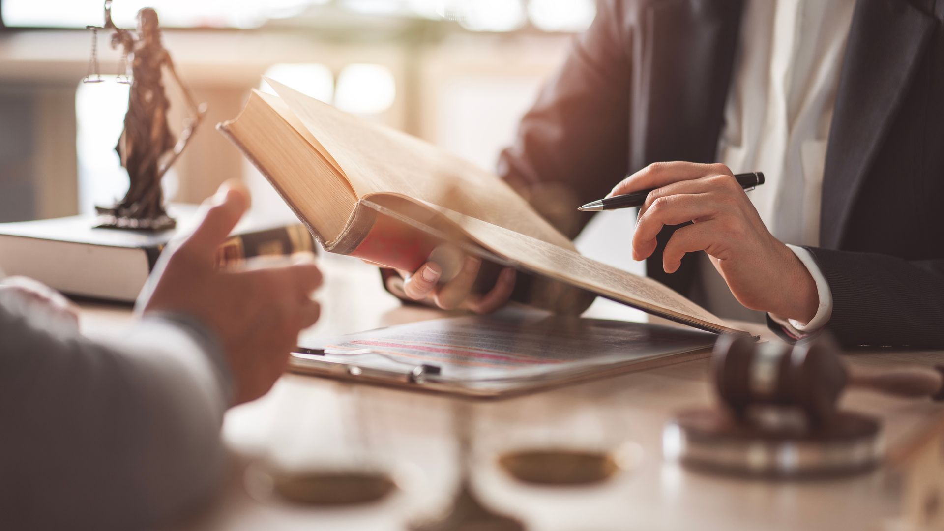 Two people discussing a book at a desk with legal symbols.