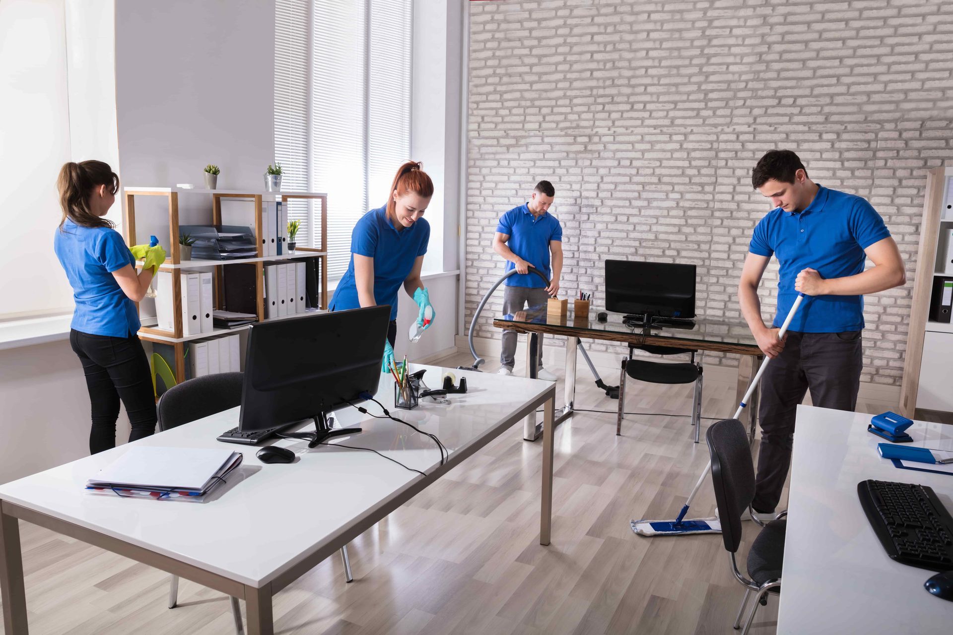 Group Of Janitors Cleaning The Modern Office With Caution Wet Floor Sign