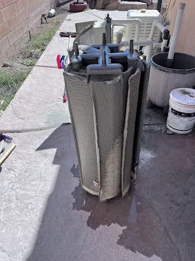 A cylindrical pool filter cartridge on a concrete surface, partially disassembled, showing its pleated filter media.