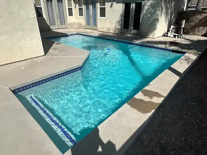 Swimming pool with turquoise water, surrounded by a concrete patio and building.