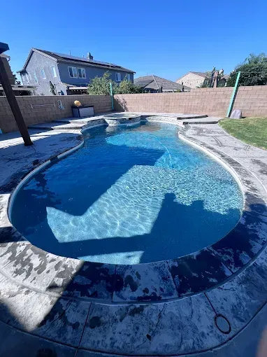 A blue, kidney-shaped swimming pool in a backyard on a sunny day.