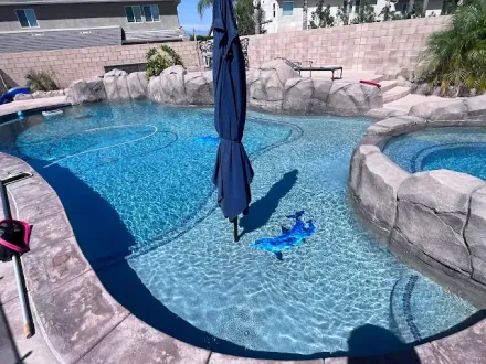 A swimming pool with clear blue water and an umbrella in the center.