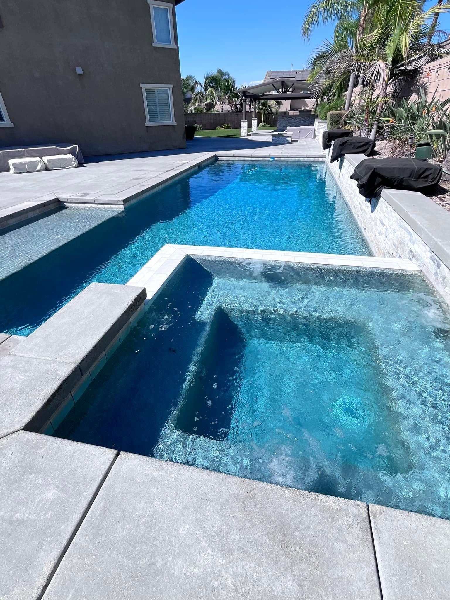 Swimming pool and spa with turquoise water surrounded by stone patio.