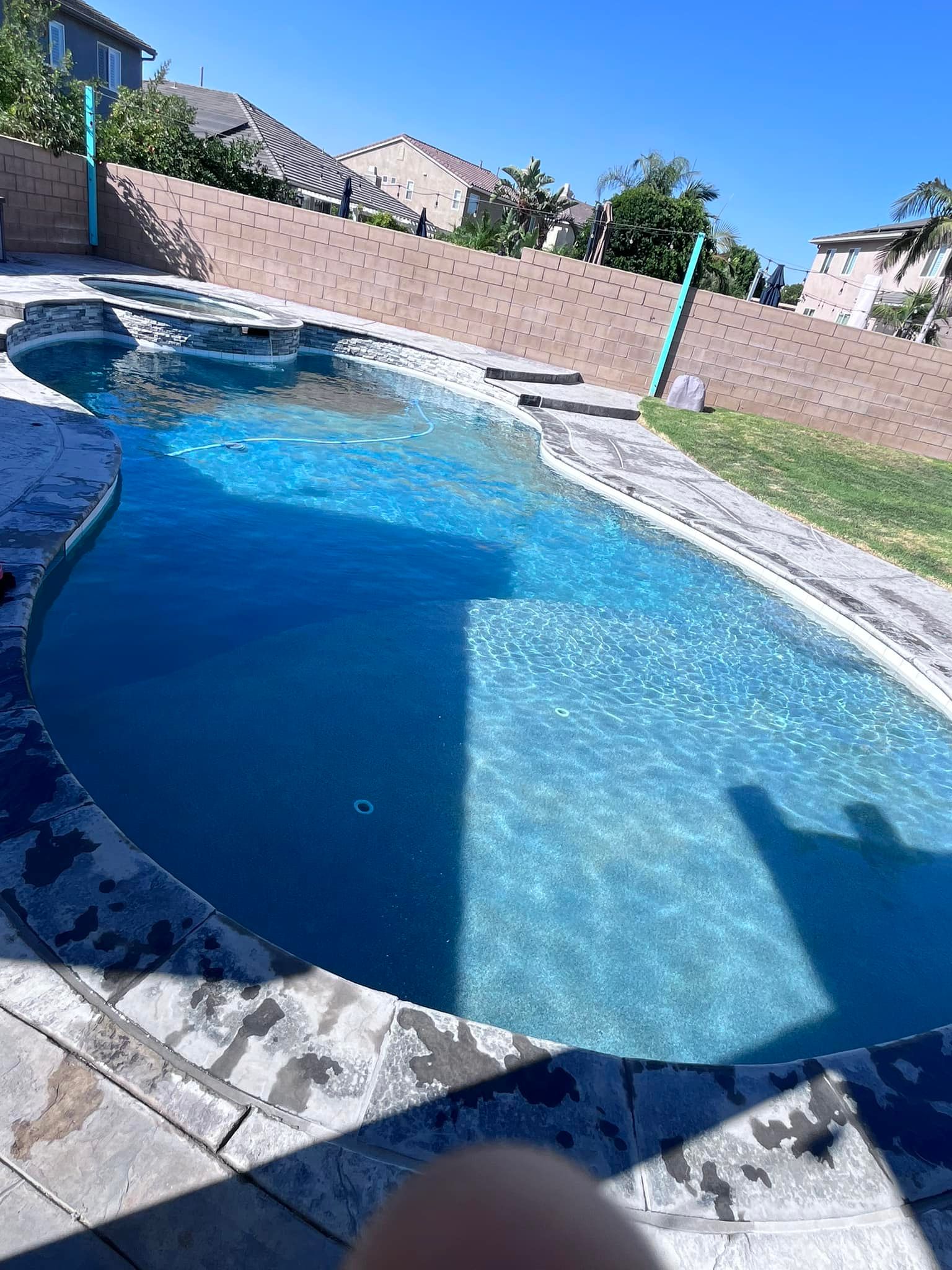 Swimming pool with turquoise water, surrounded by stone and a retaining wall on a sunny day.