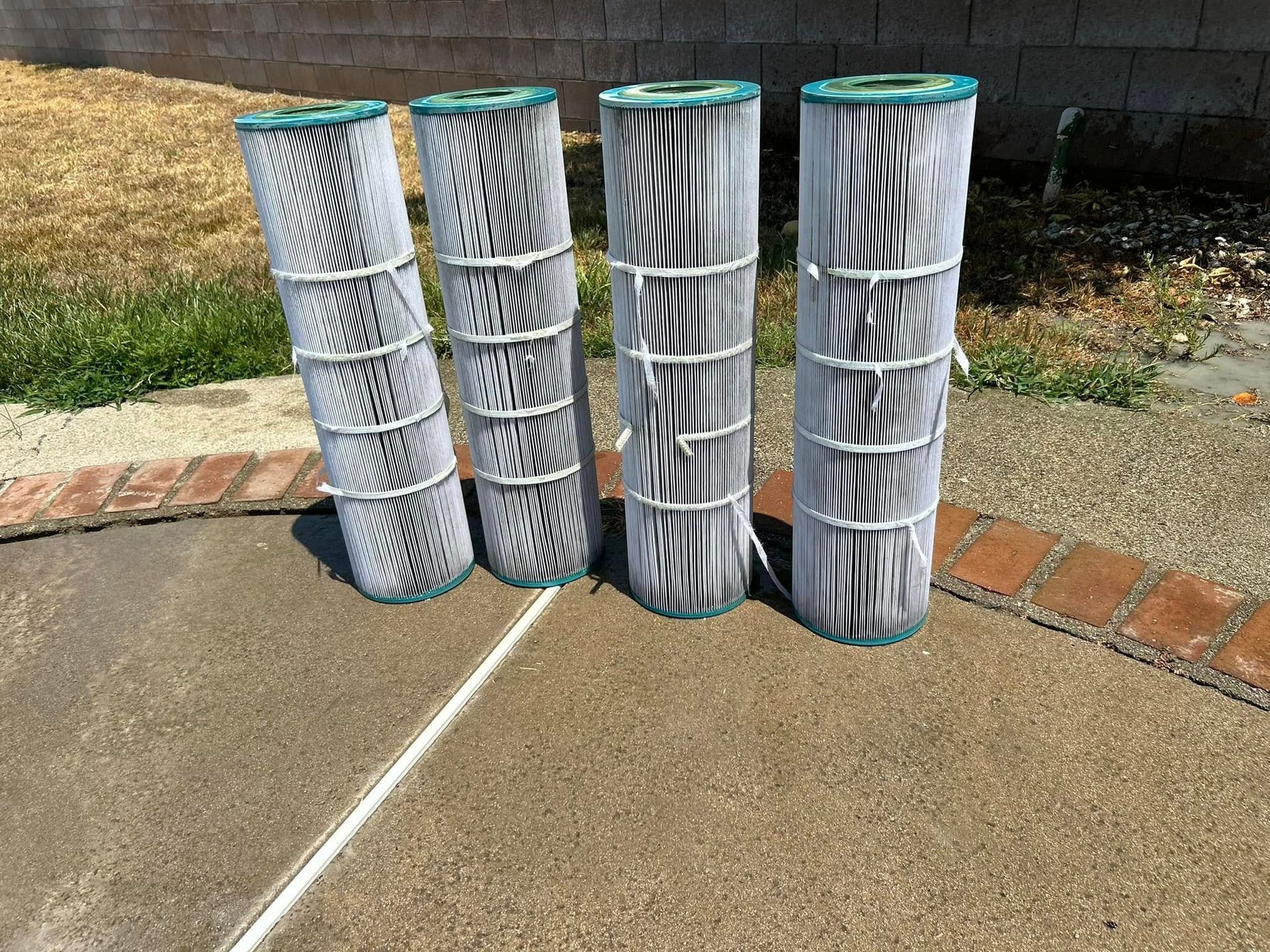 Four cylindrical pool filters standing on a concrete surface next to a brick border.