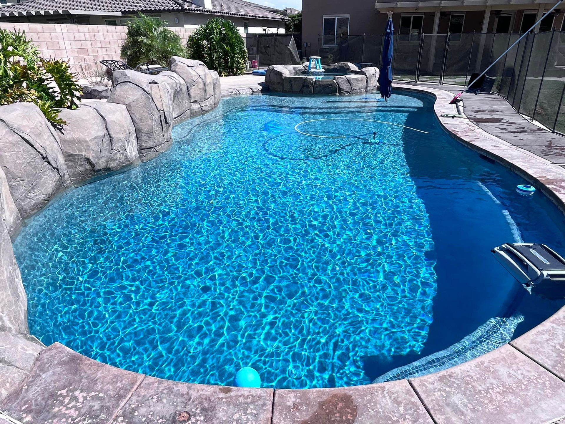 A sparkling blue swimming pool with rock waterfall feature and sun shade umbrella.