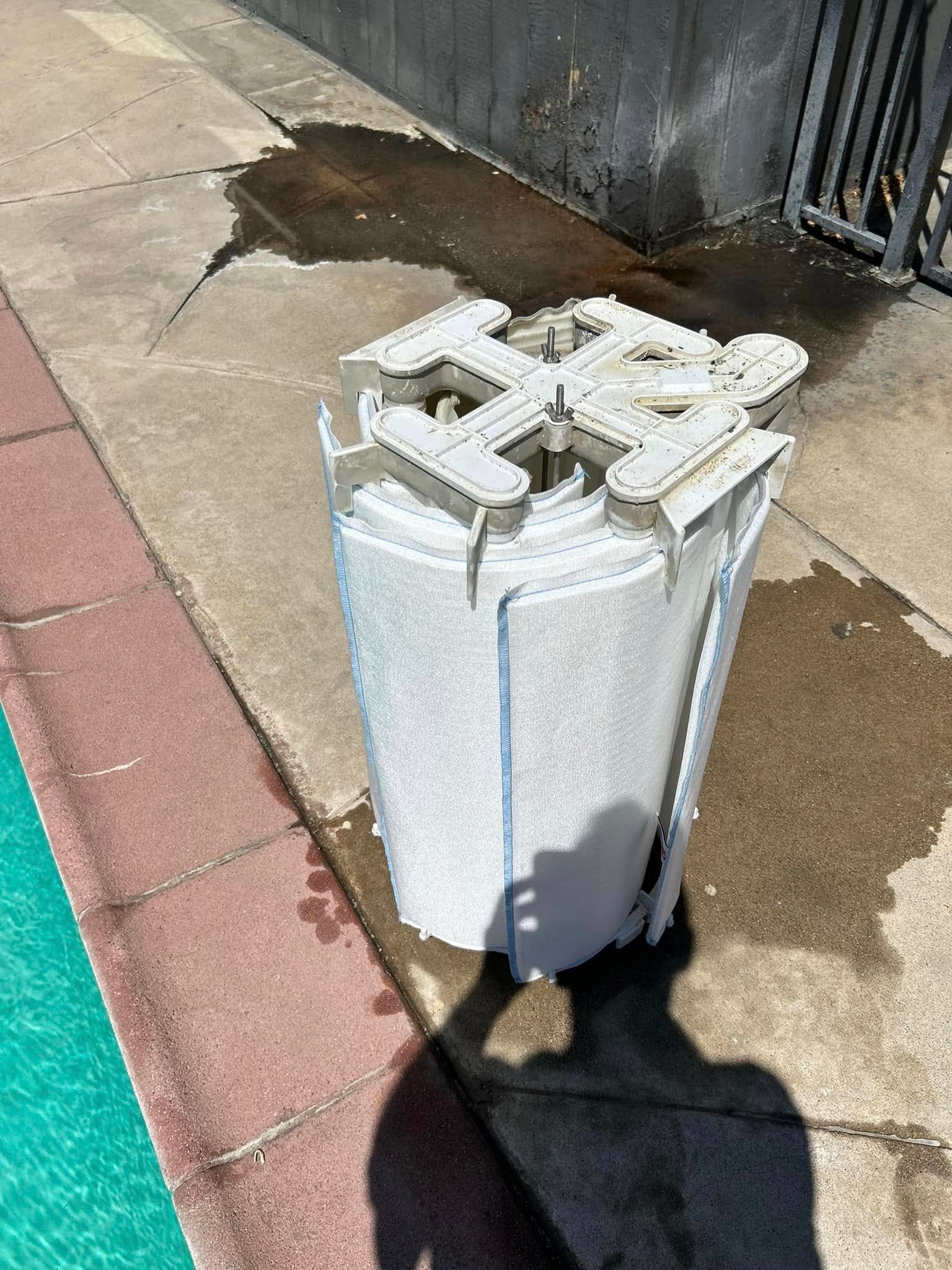 Rolled-up white filter with a plastic top, sitting on concrete near a pool. Shadow of a person present.