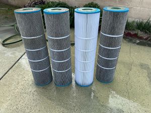 Four pool filter cartridges standing on a wet surface, three gray and one white.