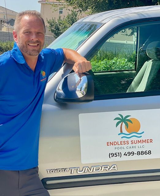 Woman in straw hat smiles, holding wine glass near a lake.