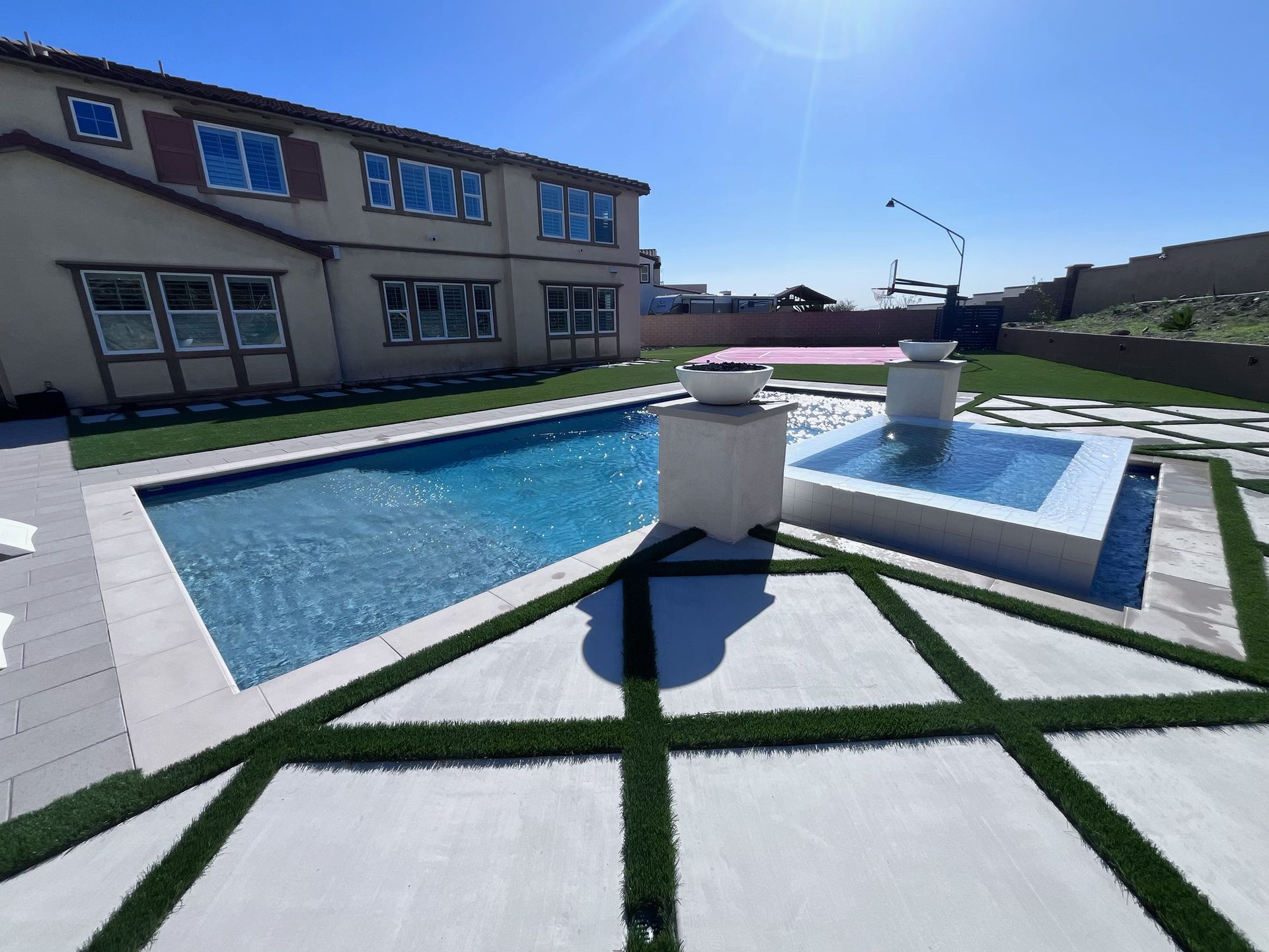 Backyard with a swimming pool, hot tub, and stone patio with artificial grass accents.