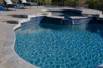 Swimming pool with blue water and surrounding stone patio; lounge chairs visible.