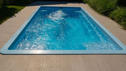 Rectangular blue swimming pool, light-blue border, surrounded by stone tiles. Water rippling inside.
