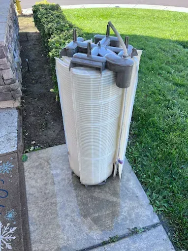 Pool filter on a concrete surface next to a lawn and building.
