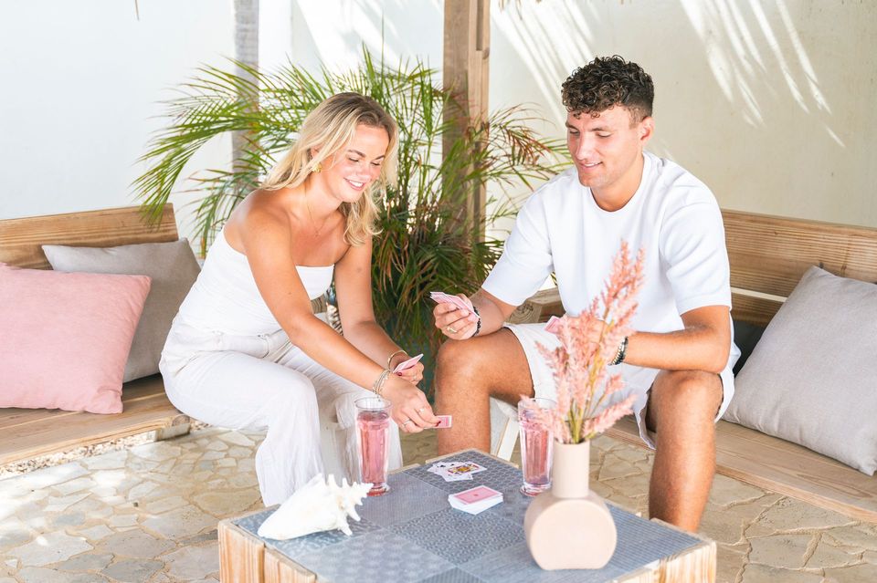 A man and a woman are sitting at a table toasting with drinks.