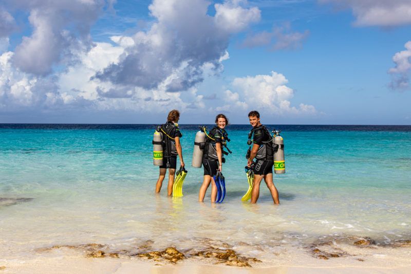 Three scuba divers are standing in the ocean on a beach.