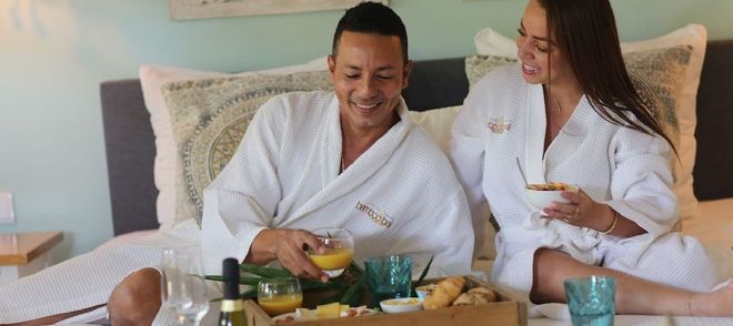 A man and a woman are sitting on a bed with a tray of food.